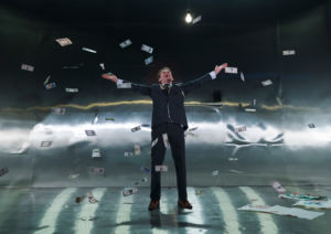 Skådespelaren Simon Reithner i karaktär som Tom Ripley, kastar upp massor av dollarsdelar i luften som regnar ner.