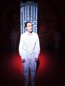 Emil Brulin i Gyllene Draken, vita byxor och vit skjorta, röd scenografi i bakgrunden