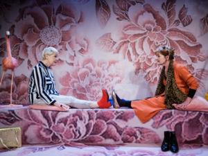 Föreställningsfoto, Ulla Tylén & Tytte Johnsson mitt emot varandra sittandes ned med rosa scenografi/bakgrund