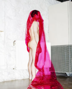 En naken man som står med ryggen till, invirad i rosa plast