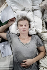 skådespelaren marika holmström ligger i en obäddadsäng med räkning i handen