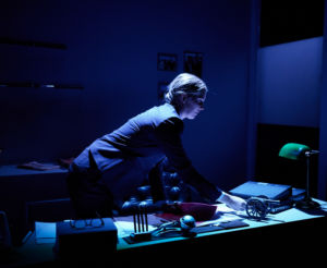 Skådespelaren Linda Kulle böjer sig över ett skrivbord i mörkret. (repetition på lilla scen)