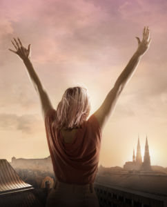 Ung tjej med rosa hår står med armarna utsträckta och blickar ut över staden Uppsala i sommarnatten