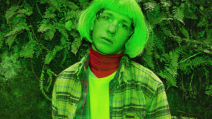 Kille med flanellskjorta och labbglasögon i grönt ljus utomhus