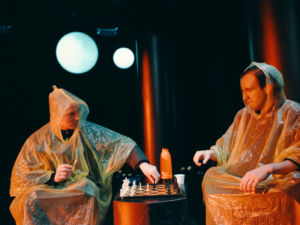 Skådespelarna Harry Friedländer och Emil Brulin i varsin orange regncape, spelar schack