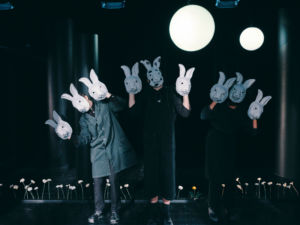 Svartklädda skådespelare med kaninmasker över ansiktet och hållandes kaninmasker i händerna