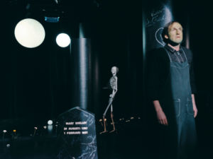 Skådespelaren Emil Brulin som Franktensteins monster,ser rädd ut. Skelett och gravsten bakom honom