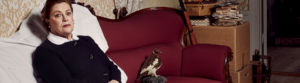 Skådespelaren Anna Carlson sitter i en övertäckt soffa i ett gammalt rum med sliten tapet, blick in i kameran. Flyttkartonger står staplade på varandra och en hund av rasen saluki ligger nedanför soffan och blickar upp mot henne.