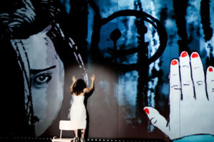 Frida Österberg med händerna mot en vägg med projektion av målning