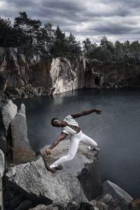 Man i vita kläder, mitt i ett danssteg på en klippa över havet