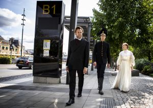 Tre personer i äldre kläder går på Uppsala busstorg
