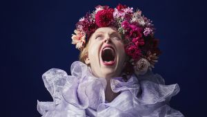 Emelie Wallberg med blomsterkrans, höjer huvudet mot skyn, gapar