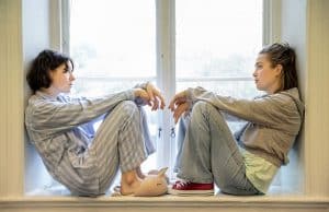två unga kvinnor titta på varandra i ett klassrum där de sitter i ett fönster