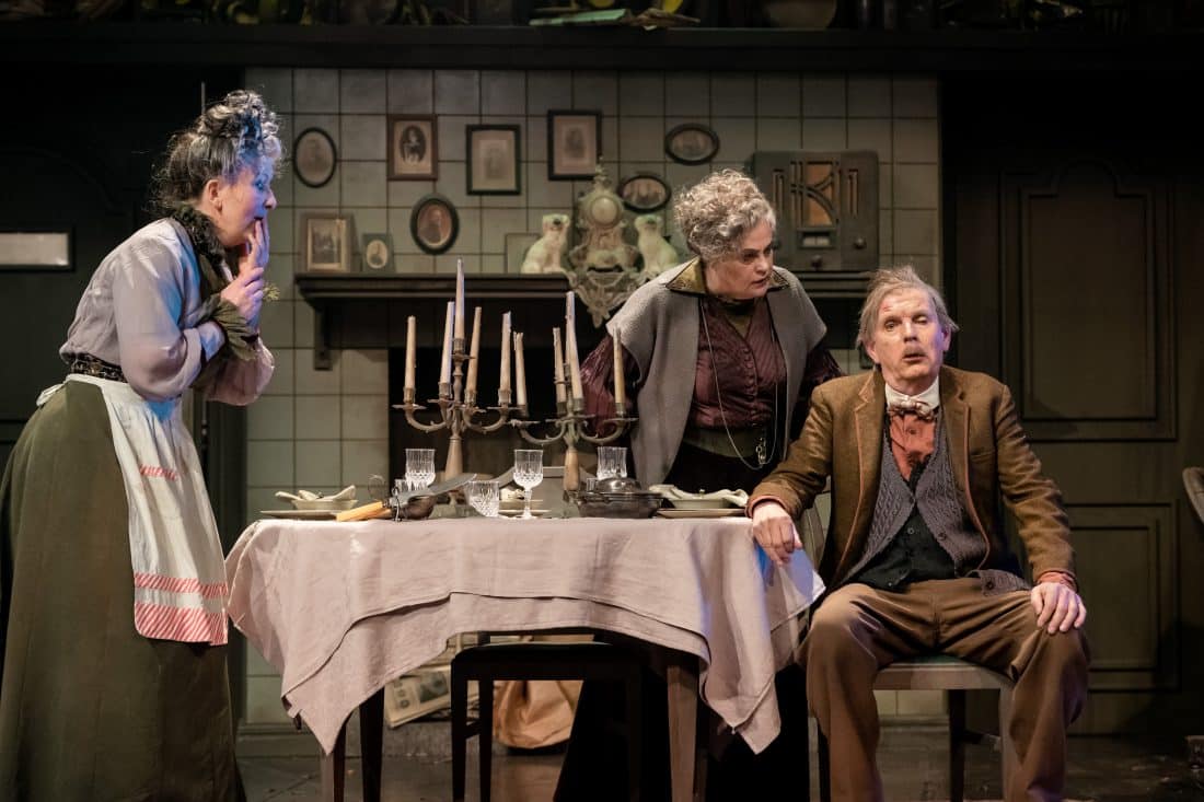 en man vid ett middagsbord och två äldre damer som passar upp