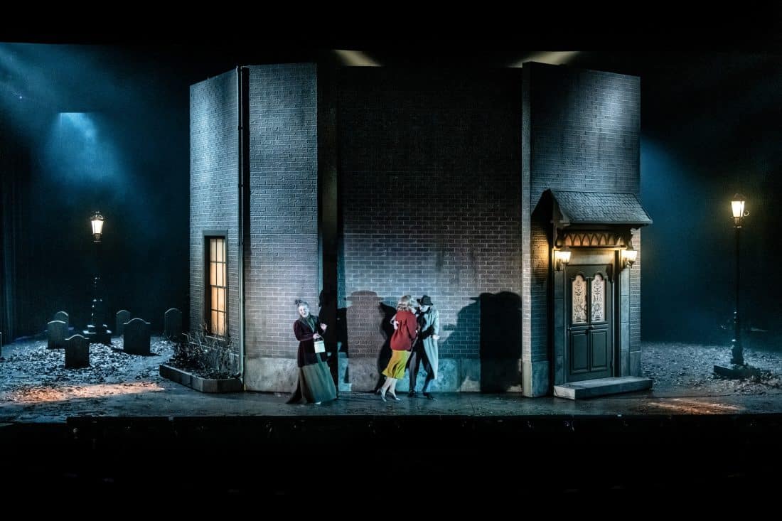 tre personer utanför ett stort hus på en scen