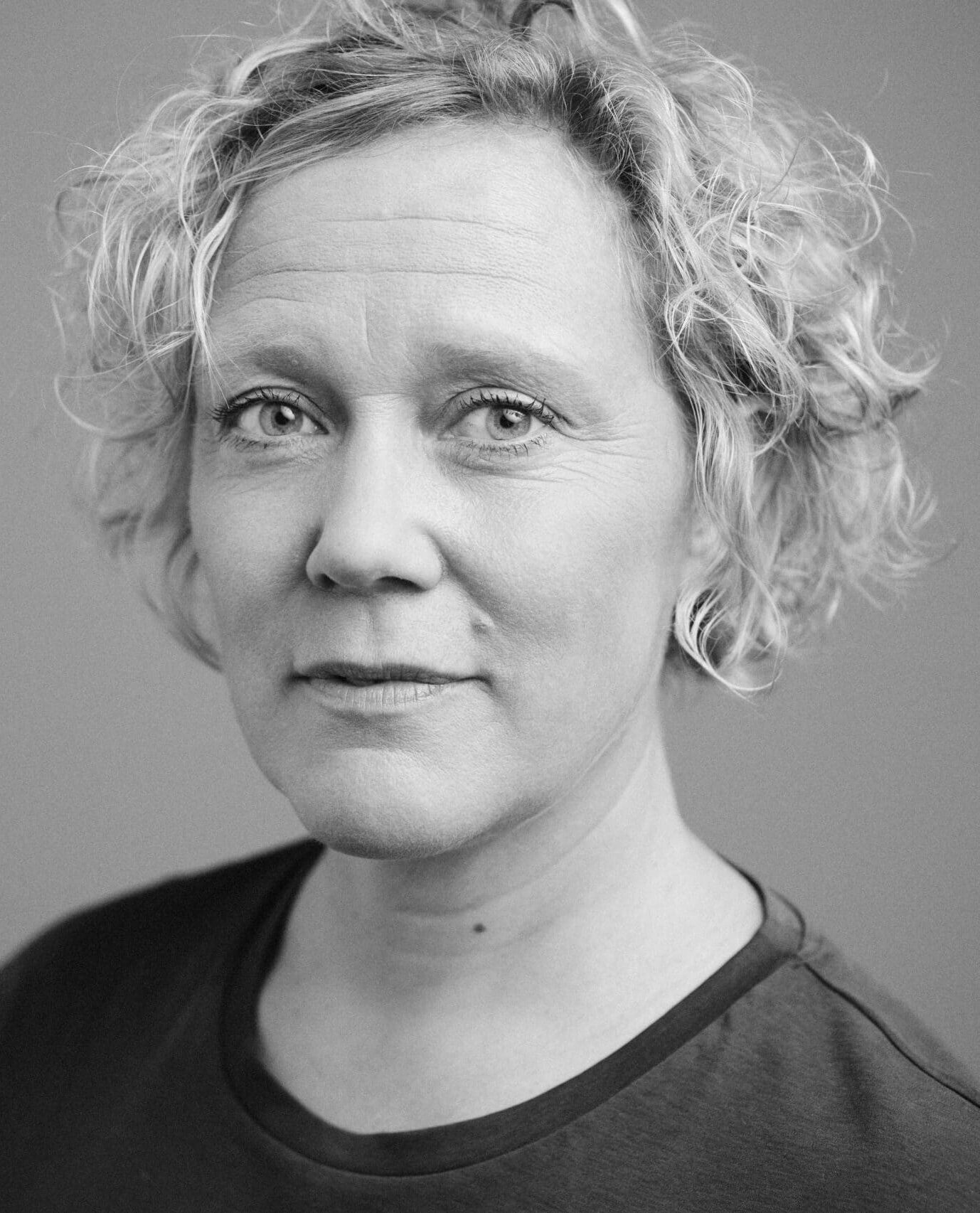 Porträtt på kvinna med ljust vågigt hår som tittar in i kameran.